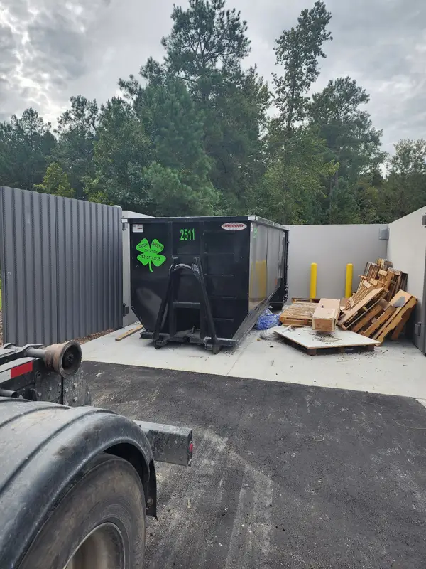Irish Greens container 2511 in a dumpster enclosure next to stacked pallets