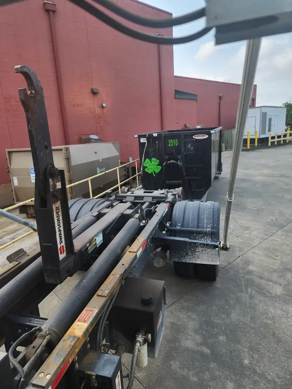 Roll-off truck lined up with Irish Greens container 2510 behind a brick building